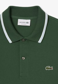 Zielona koszulka polo wykonana z teksturowanej tkaniny, z plisą na dwa guziki, kołnierzem w niebiesko-białe paski oraz małym wyszywanym logo.