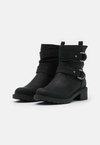 Botines negros de cuero sintético con un acabado texturizado. Presentan dos correas con hebillas de metal, un tacón bajo estilo bloque y una puntera redondeada.