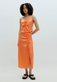 Oranges Satin-Zweiteiler-Set mit einem ärmellosen Top mit Kordelzug und einem Midirock mit Raffung und seitlichem Schlitz. Getragen mit schwarzen Sandalen.