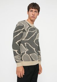 Gebreide trui met een geometrisch patroon in zwart en beige, voorzien van een ronde hals en geribbelde manchetten, gemaakt van een zachte, gestructureerde stof.