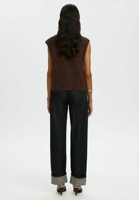 Brązowy dzianinowy bezrękawnik, czarne szerokie dżinsowe spodnie z szarymi mankietami oraz czarne szpilki, widok z tyłu.