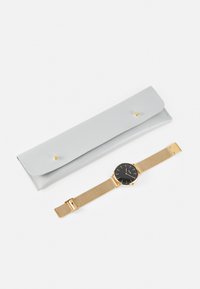 Montre noire avec bracelet en mailles dorées à côté d'un étui en cuir gris avec fermeture à pression et logo embossé.