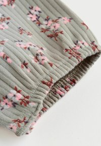 Svetlo siva rebrasta tkanina z rožnatim in rjavim cvetličnim vzorcem ter elastičnim manšetom na belem površju.