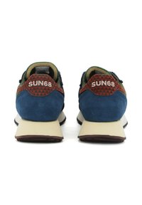Blaue Wildledersneaker mit schwarzen Akzenten und einem gemusterten roten Absatz. Der Schuh hat eine beigefarbene Sohle mit leichter Erhöhung. Logo am Absatz sichtbar.