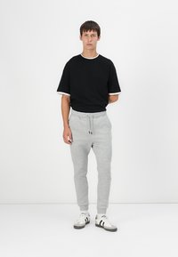 Black short-sleeve t-shirt with white trim, paired with gray sweatpants featuring an elastic waistband and cuffs, complemented by white and gray sneakers.