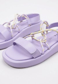 Sandalias de plataforma moradas con correas delgadas y lazos decorativos. Material sintético suave y suela acolchada para mayor comodidad.