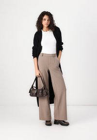 Svart lang cardigan, hvit topp, beige høyspent vide bukser og brun lærhåndveske. Kraftige brune sko fullfører antrekket.