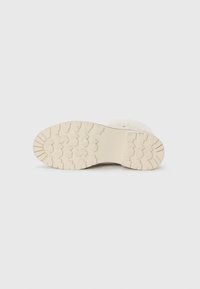 Semelle de botte à fourrure blanche avec une prise en caoutchouc texturée, présentant un design massif et des motifs de traction proéminents pour la durabilité.