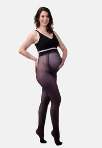 Collants de soutien noirs pour femmes enceintes avec une texture transparente, taille haute et une ceinture renforcée, présentés par un mannequin en bralette noire.