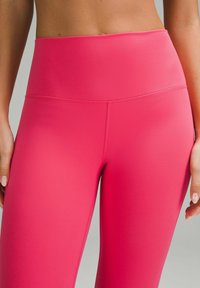 Růžové legíny s vysokým pasem vyrobené z elastického materiálu s hladkým povrchem. Mají bezešvou střední část a žádné viditelné kapsy nebo kovové prvky.