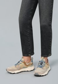 Beige a světle hnědé tenisky vyrobené z nubuku a síťoviny, s modrými tkaničkami, šedou gumovou podrážkou a dekoračními akcenty. Nosené s tmavými džíny.