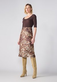 Smeđa, uska majica u kombinaciji s leopard uzorkovanom A-linijom suknjom; do koljena, glatki materijal. Nošena s bež, visokim čizmama.