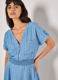 Vestido de chambray azul claro con mangas cortas, escote en V profundo, dos bolsillos en el pecho y una cintura fruncida para un ajuste relajado.