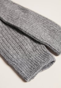 Prenda de punto acanalado gris con una textura suave, que presenta extremos alargados y cónicos, y un dobladillo ligeramente deshilachado a lo largo de los bordes.