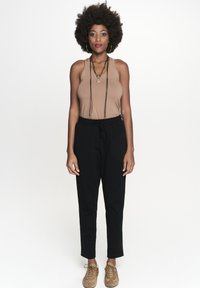 Brązowy top na ramiączkach, czarne spodnie i beżowe buty. Modelka z kręconymi włosami nosząca długi naszyjnik. Prosty design i neutralne kolory.