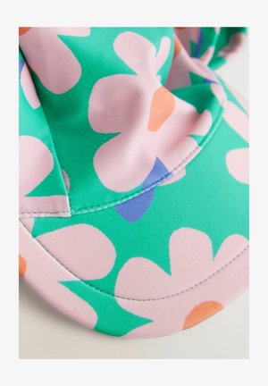 Vihreä hattu, jossa on suurikokoinen vaaleanpunainen kukkakuosi ja oranssit yksityiskohdat. Silkkinen kangas, jossa on näkyvät saumat lierissä ja kruunussa.