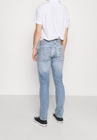 Vaqueros de mezclilla azul claro con un diseño de pierna recta. Presentan costuras en contraste y bolsillos traseros clásicos, combinados con zapatillas negras.