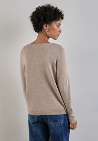 Maglione in maglia beige con scollatura ampia, maniche lunghe, orli a coste e una vestibilità rilassata, indossato su jeans blu. Texture morbida e design leggero.