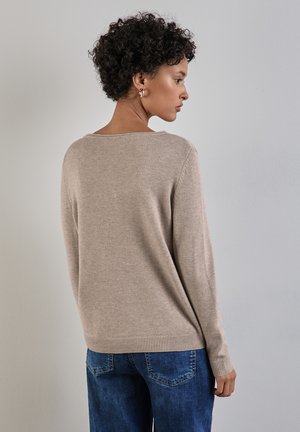 Maglione in maglia beige con scollatura ampia, maniche lunghe, orli a coste e una vestibilità rilassata, indossato su jeans blu. Texture morbida e design leggero.
