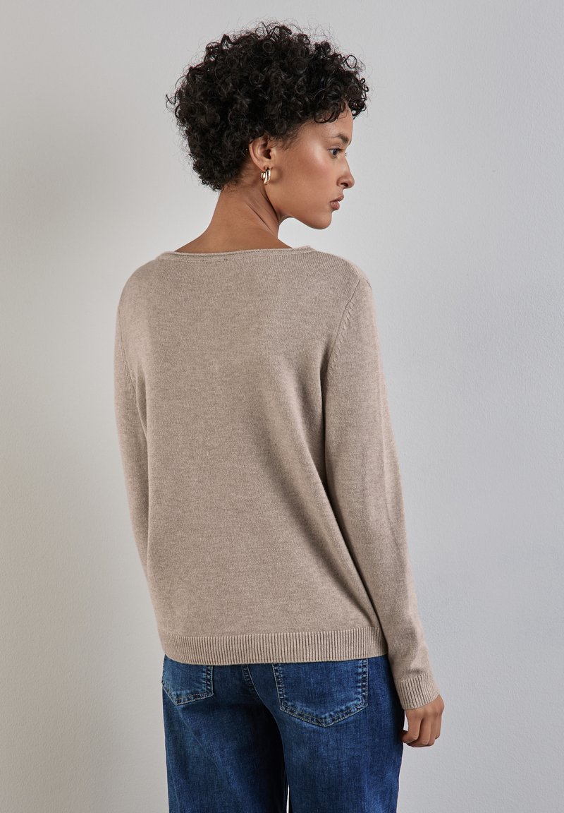Maglione in maglia beige con scollatura ampia, maniche lunghe, orli a coste e una vestibilità rilassata, indossato su jeans blu. Texture morbida e design leggero.