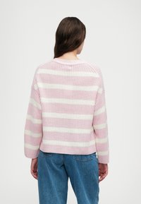 Suéter de malha listrado em rosa e branco com um corte descontraído, gola canelada e ombros caídos, combinado com jeans de denim azul claro.