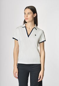 Polo bianco con rifiniture blu navy, maniche corte, scollatura a V e un piccolo logo ricamato sul petto. Materiale in cotone liscio.