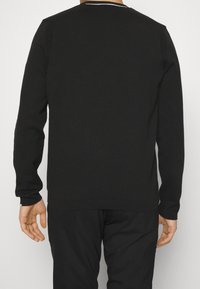 Pull noir tricoté à manches longues, accents côtelés aux épaules, et col rond, vu de dos. Texture douce.