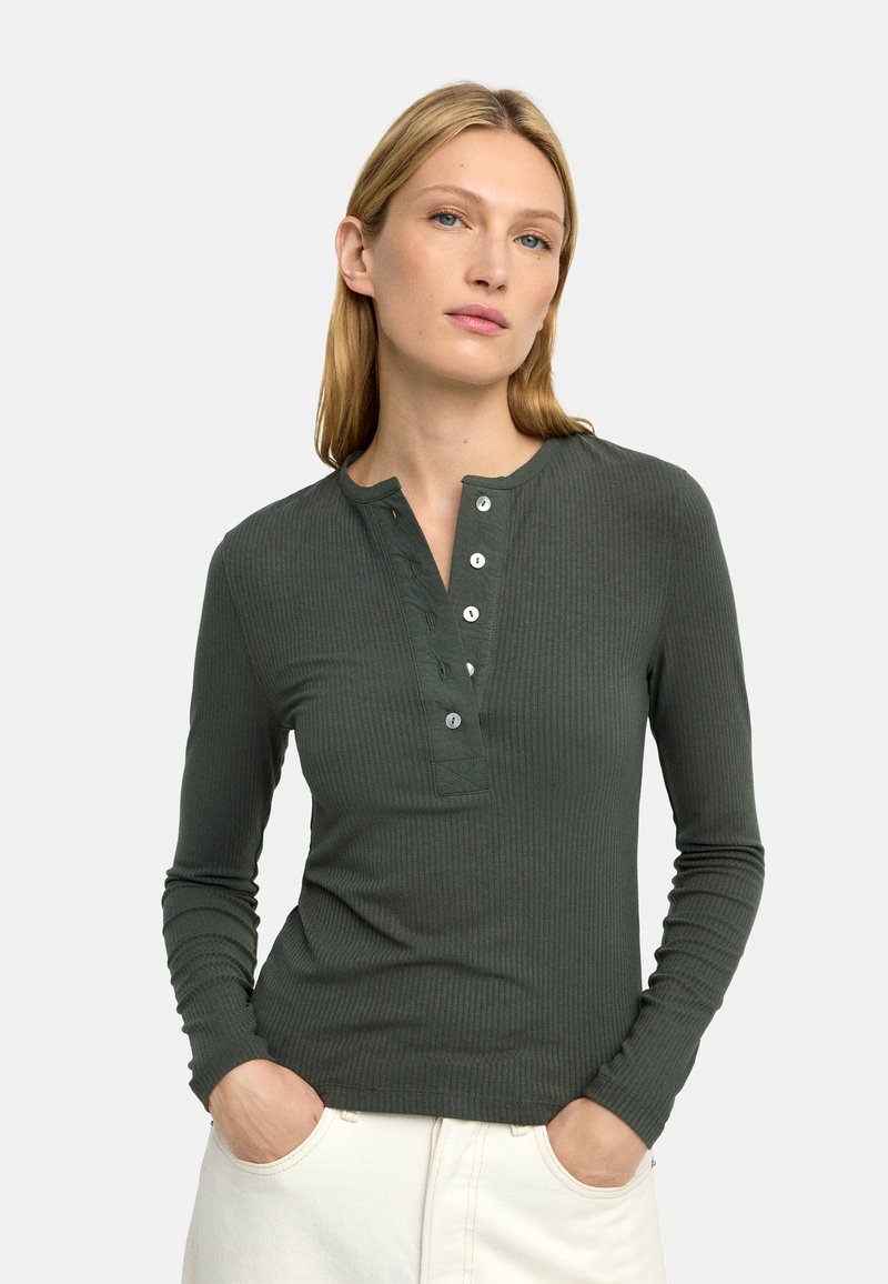 Ciemnozielona, prążkowana bluzka z długim rękawem, z kołnierzykiem henley, plisą z guzikami z pięcioma guzikami oraz dopasowanym fasonem.