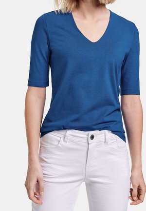 Blå kortærmet V-hals T-shirt lavet af blødt stof, kombineret med hvide denimjeans med knaplukning og lommer.