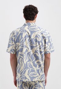 Korte mouwen shirt in lichtblauwe stof met grote crèmekleurige abstracte bladvormen. Heeft een kraag en een ontspannen pasvorm.