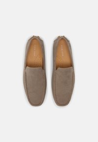 Paire de mocassins taupe en daim à enfiler avec des détails cousus et des semelles intérieures rembourrées couleur tan portant la marque "Pier One" sur un fond blanc.