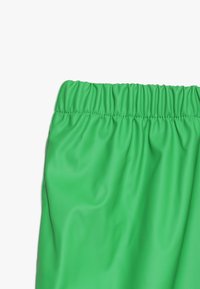 Bermudas verdes com cós elástico, feitas de um material suave e brilhante, apresentando uma cintura franzida com uma textura subtil e sem padrões visíveis.