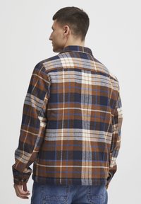 Checkered flannel shirt in brown, navy, and cream. Features button cuffs and a spread collar. Soft texture and relaxed fit.