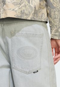 Svetlomodré riflové krátke nohavice s vreckom na zadnej strane s vyrazeným logom Adidas, kontrastným šitím a malou čiernou štítkom na leme.