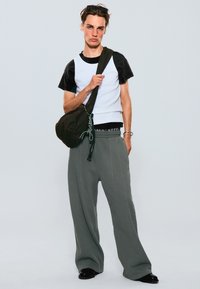 Top alb și negru cu mâneci scurte, pantaloni gri cu talie largă și o geantă maro cu șnur. Pantofi negri, design în straturi, stil minimalist.