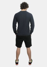 Maglione blu navy in tessuto a maglia, indossato con pantaloni corti neri, visto da dietro. Le scarpe presentano accenti arancioni e verdi. Vestibilità casual.