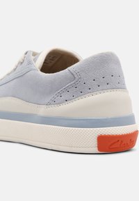 Světle modré semišové tenisky s bílou gumovou podrážkou, která má texturovaný vzor, světle modrý akcentní pruh a oranžové logo na patě.