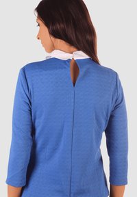 Blusa de textura azul con cuello blanco, mangas tres cuartos y detalle de ojal en la espalda. La tela tiene un patrón sutil.