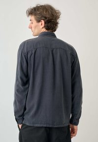 Dunkelgraues Langarmshirt mit Knopfkragen, das eine entspannte Passform und eine dezente Textur aufweist, von hinten präsentiert.