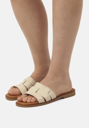 Sandali infradito di colore crema con design intrecciato, suola piatta e accenti marroni. Materiale liscio e resistente con una calzata comoda.