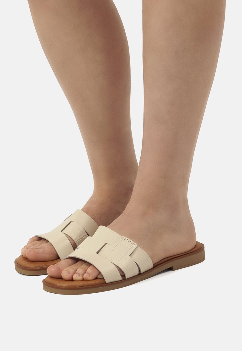 Sandali infradito di colore crema con design intrecciato, suola piatta e accenti marroni. Materiale liscio e resistente con una calzata comoda.