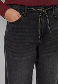 Dunkelgraue Denim-Jeans mit lockerer Passform, ausgestattet mit einem Kordelzugverschluss, Fronttaschen und einer subtilen Textur.