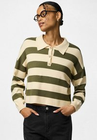 Sweter w zielono-kremowe paski z kołnierzykiem, plisą na cztery guziki oraz ściągaczami na mankietach, zestawiony z czarnymi spodniami. Miękka dzianinowa faktura.