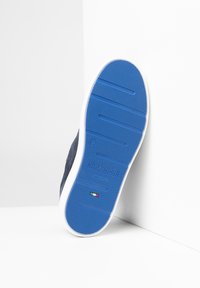 Suola in gomma blu con presa texture, intersuola bianca e parte superiore scura con texture. Marchio "NeroGiardini" in rilievo vicino al tallone. Fabbricato in Italia.