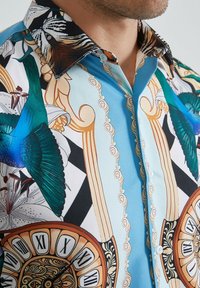 Chemise col montant avec un imprimé coloré présentant des oiseaux bleus, de grands cadrans d'horloge ornés avec des chiffres romains et des motifs enroulés décoratifs.