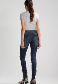 Jeans oscuros ajustados con una altura media, diseño de cinco bolsillos y un leve desgastado. Combinados con una blusa gris y botas con estampado de guepardo en blanco y negro.
