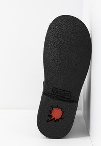 Black rubber sole with a textured finish, featuring a red accent in a splash shape. Branding visible at the heel.