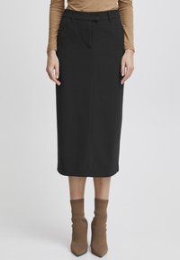 Jupe midi noire avec une coupe droite, des plis à l'avant et des passants de ceinture. Associée à des chaussettes en maille marron jusqu'à la cheville et des talons aiguilles.