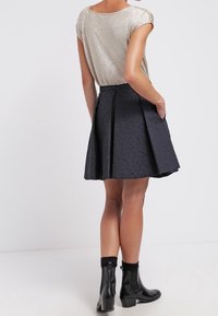 Metallisk guldig kortärmad topp kombinerad med en texturerad svart plisserad kjol. Svarta ankelstövlar fulländar looken.