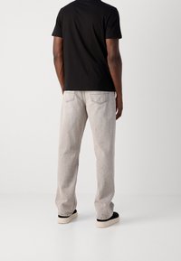 Černé tričko s krátkým rukávem v kombinaci s světle šedými džíny. Džíny mají volný střih a viditelné švy, spolu s černými botami na krémové podrážce.